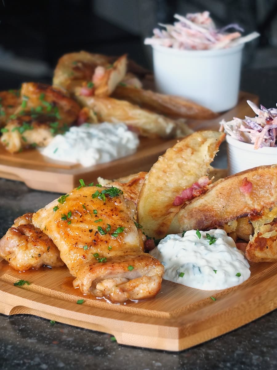 Spicy honey glazed chicken thighs on a wooden gastro pub board with cheesy bacon potato wedges, blue cheese dip and coleslaw.