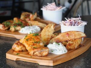 Image of wooden pub style platter with spicy honey roast chicken thighs, potato wedges, blue cheese dip and coleslaw.
