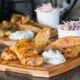 Image of wooden pub style platter with spicy honey roast chicken thighs, potato wedges, blue cheese dip and coleslaw.