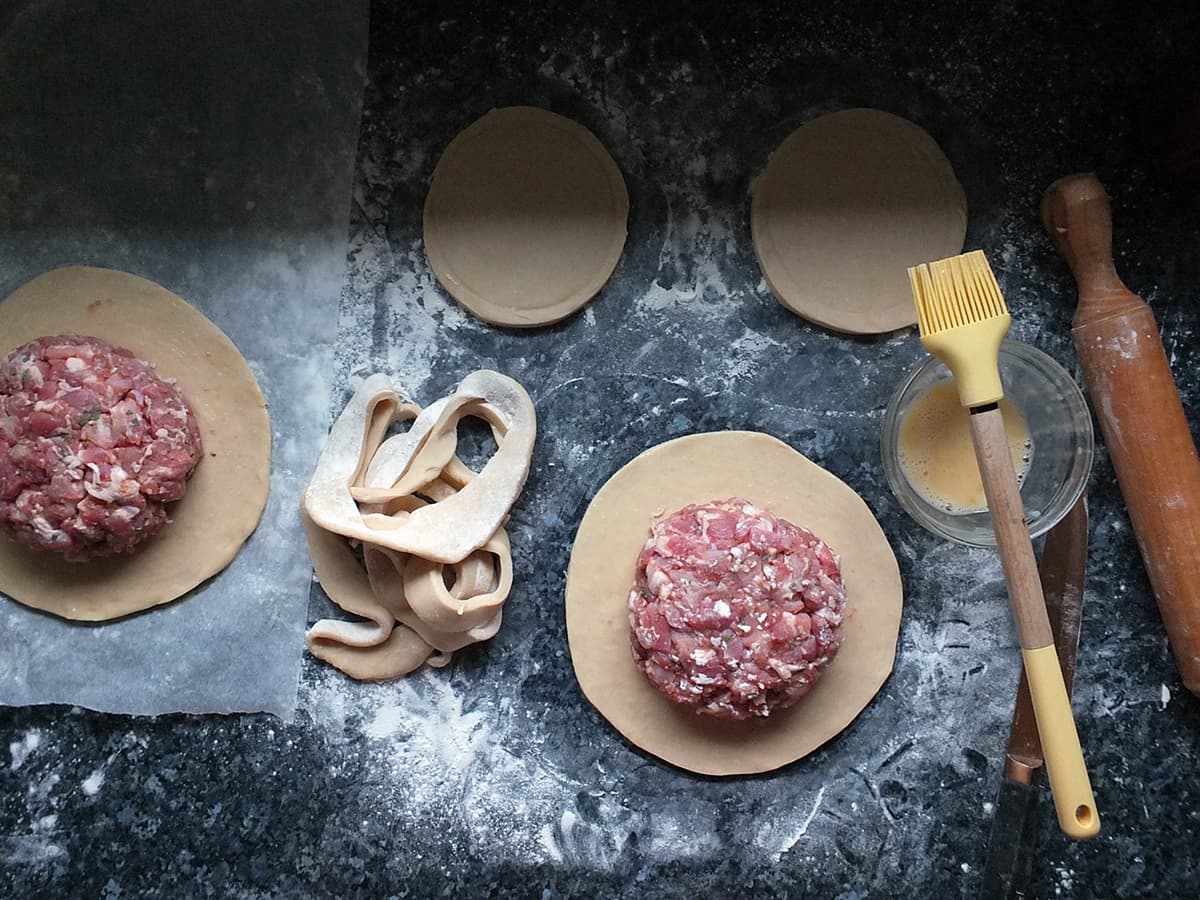 Image of hot water crust pastry rolled out and cut into circles with shaped pork pie filling on top.