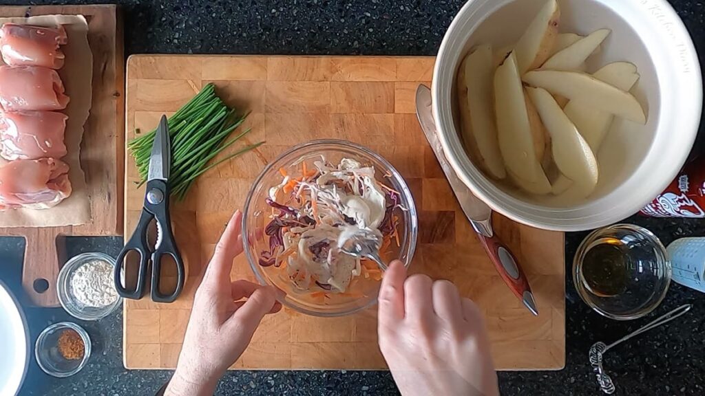 Image of hands stirring coleslaw ingredients in a glass bowl.