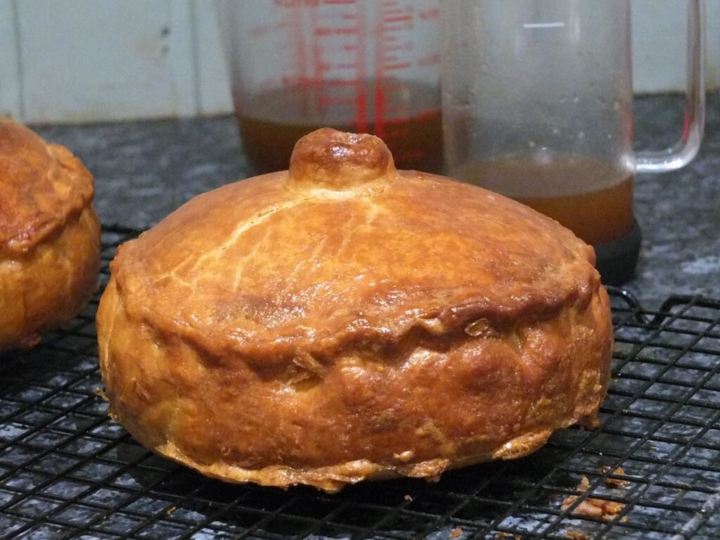 Image of cooked pork pie with a pint measuring jug in the background with cooled pork jelly in it.