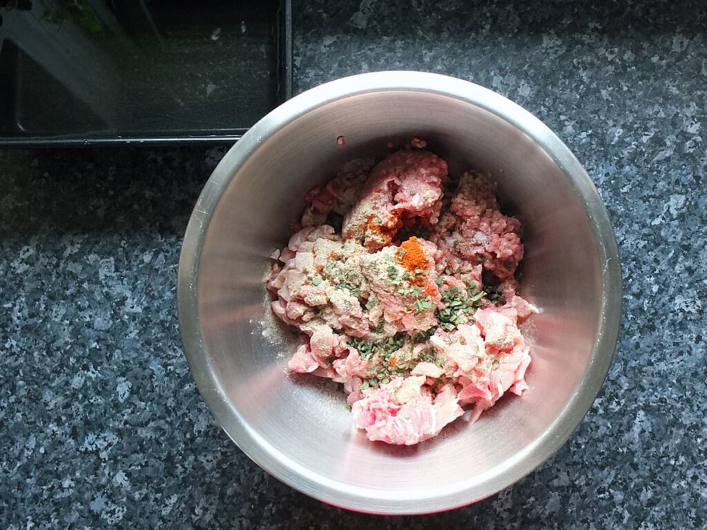 Top down image of a mixing bowl with pork and spices in it.