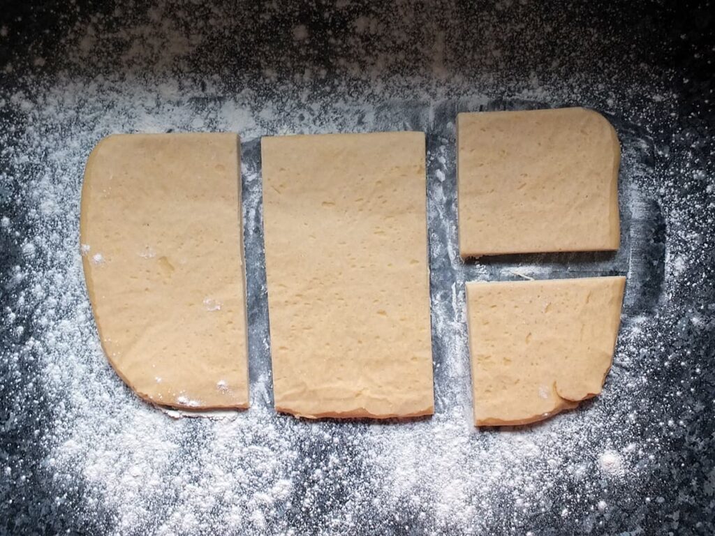 Image of hot water pastry cut into four pieces on a floured surface.