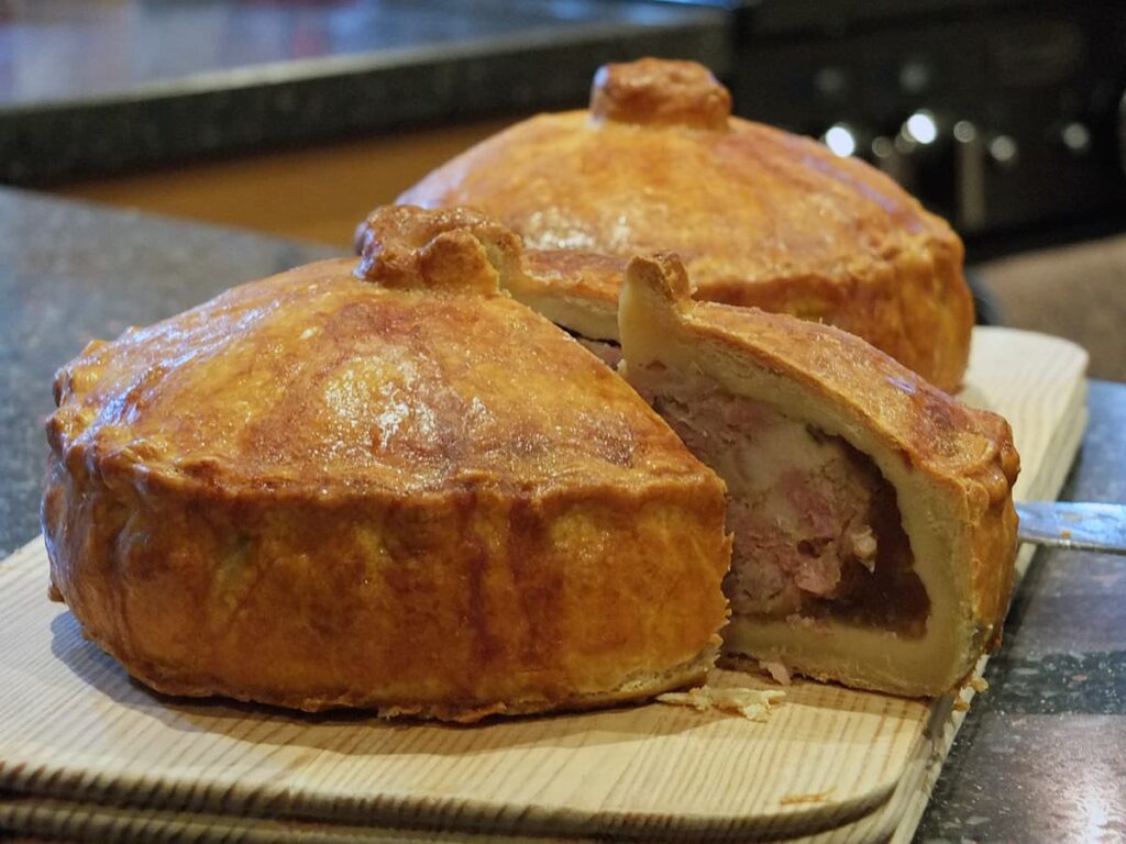Side view of pork pies with a slice cut out of one showing the layers of pork filling and pork jelly.