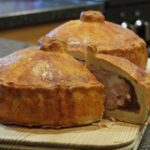 Side view of pork pies with a slice cut out of one showing the layers of pork filling and pork jelly.