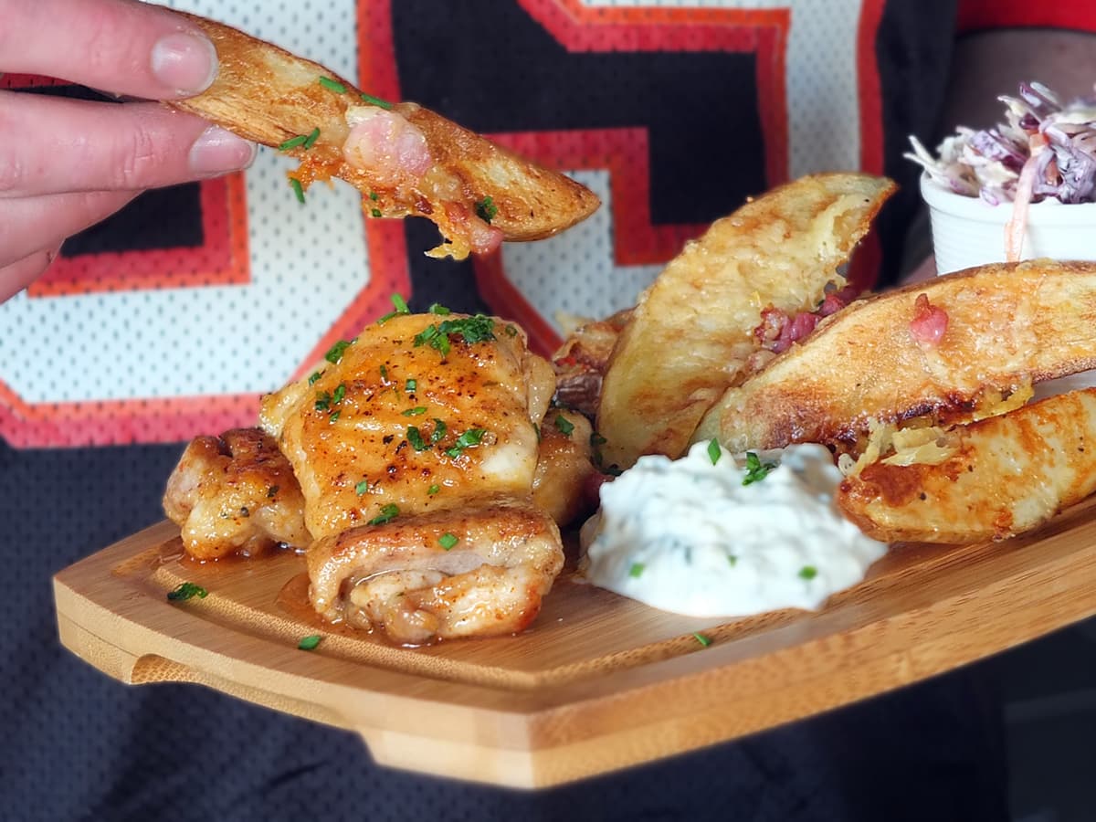 Image of man wearing football jersey while holding wooden platter with Superbowl food in one hand and a potato wedge in the other.