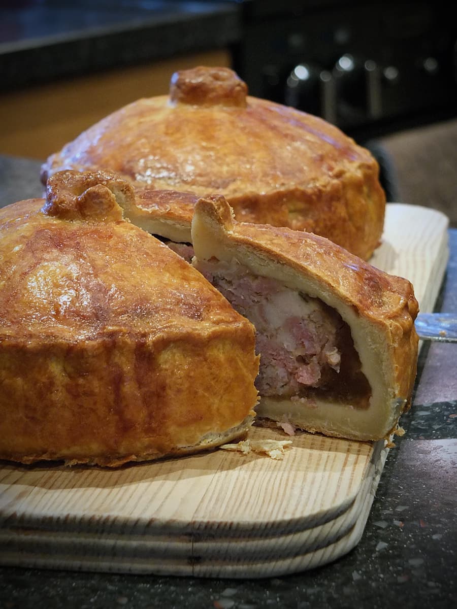 Image of two traditional British pork pies one with a slice cut out of it to show the meaty insides.