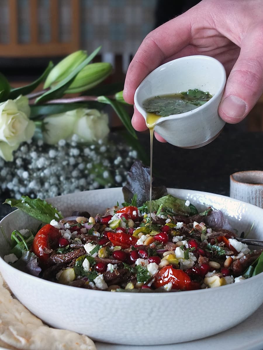 Image of man's hand pouring coriander vinaigrette from a bowl over a plate of salad.