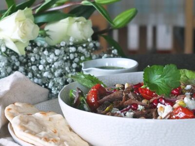 Image of crispy lamb salad in white bowl with pretty white roses and flowers in the background.