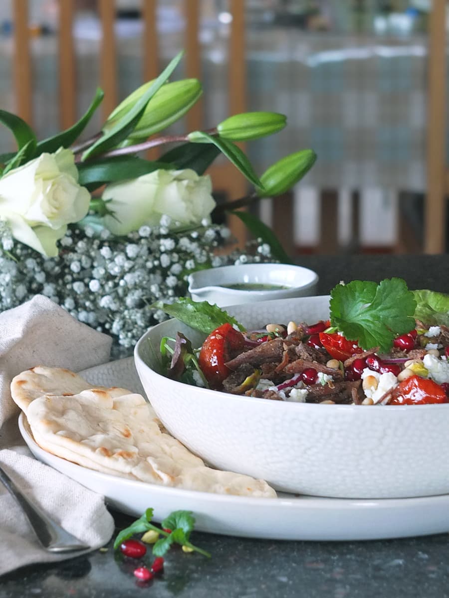 Image of crispy lamb salad in white bowl with pretty white roses and flowers in the background.