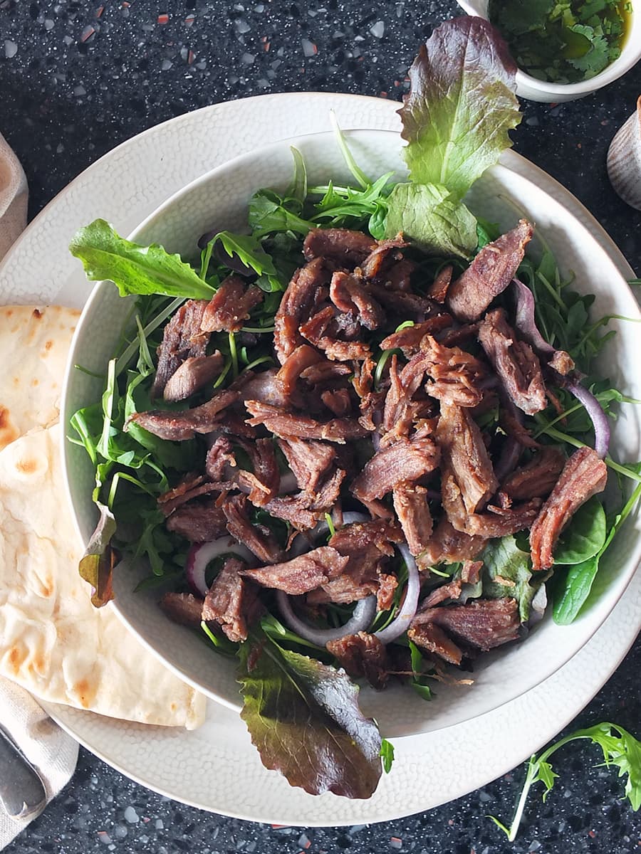 Top down image of crispy lamb on a bed of salad leaves in a bowl.