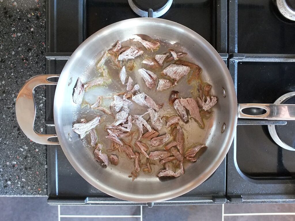 Image of shredded lamb frying in saute pan.