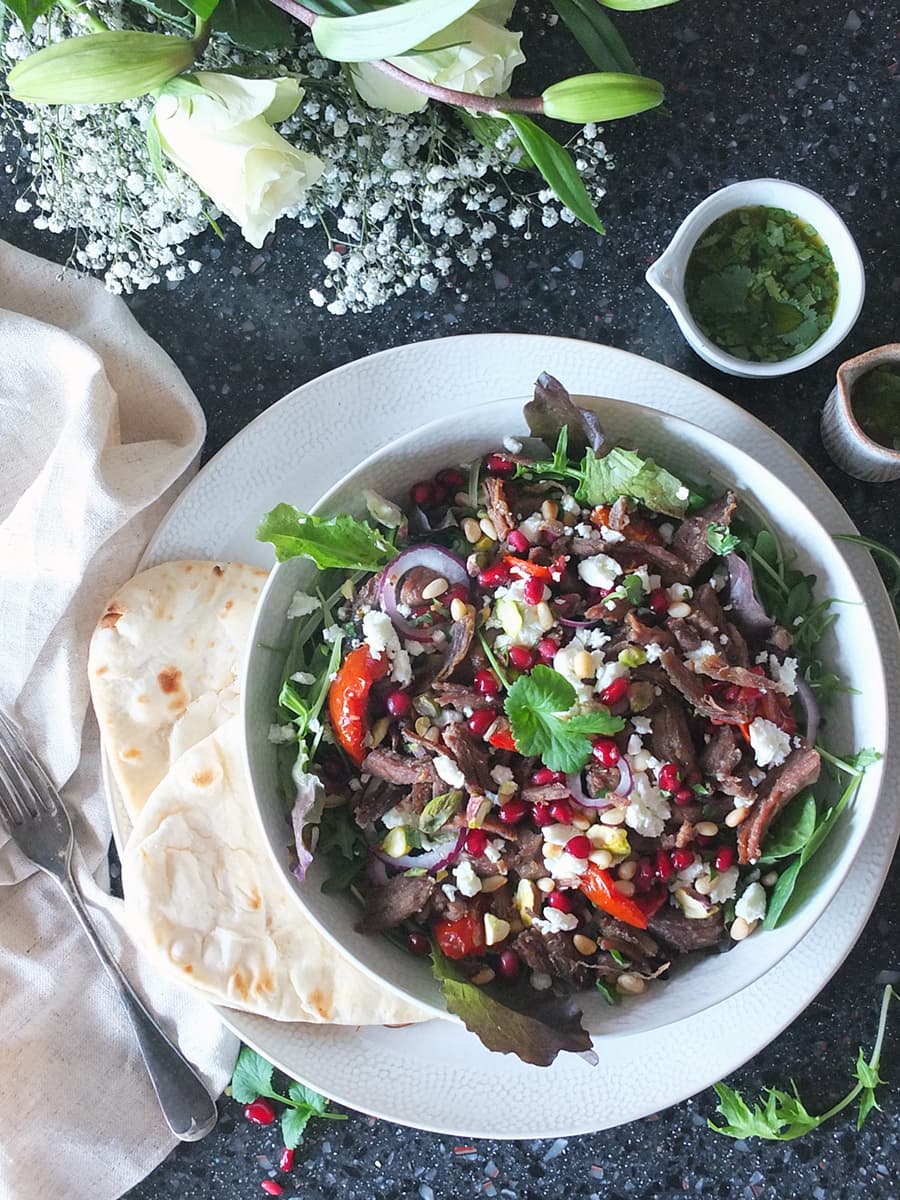 Top down image of lamb salad with flatbreads on the side and two small bowls of vinaigrette as decoration.