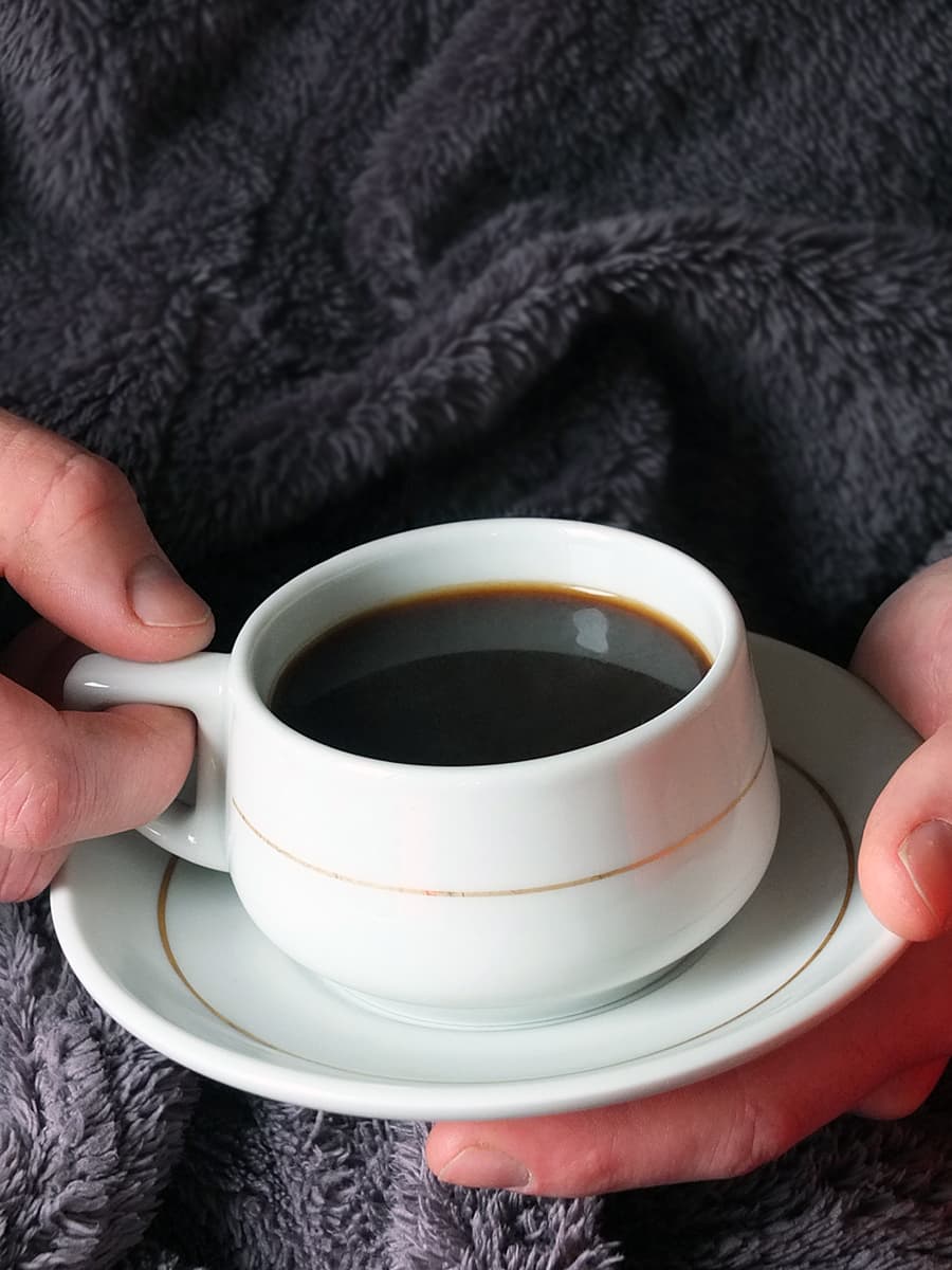Image of man in a grey bathrobe holding a cup of black coffee in his hands.