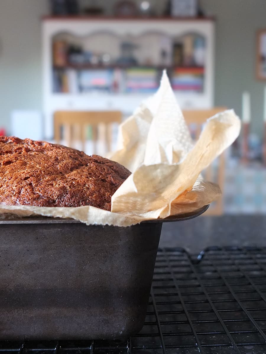 Close up image of banana bread in a loaf tin cooling on the countertop.