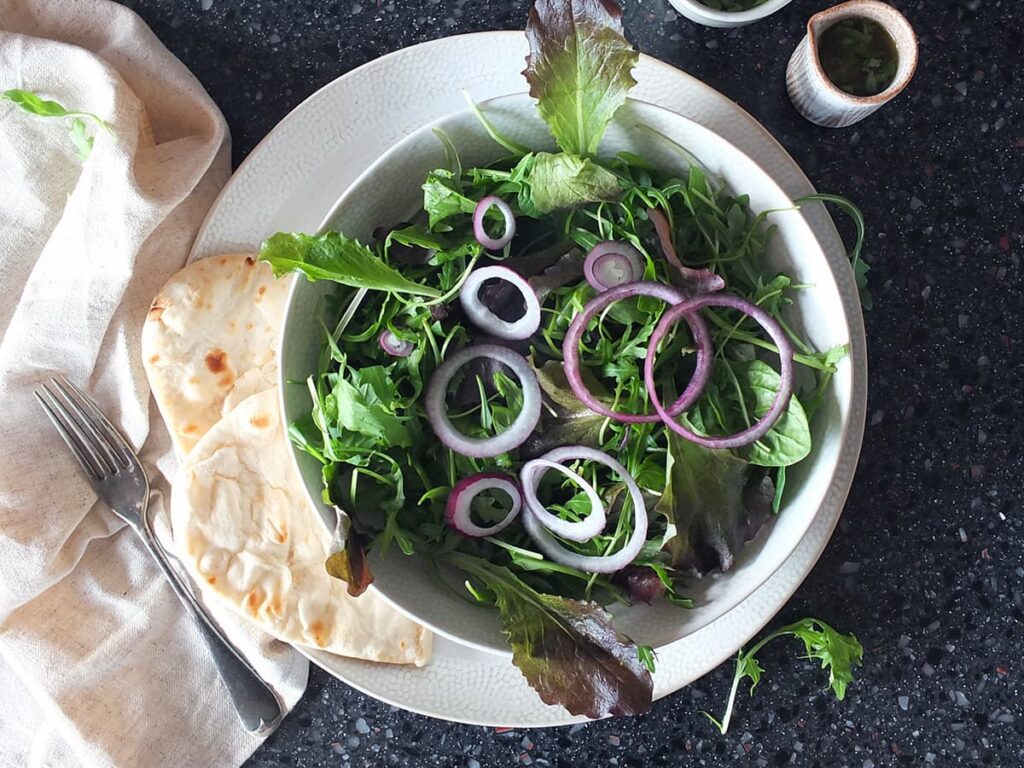 Image of onion rings layered over salad leaves in bowl.
