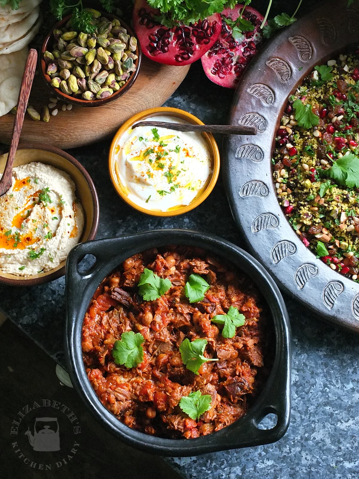 A top down Moroccan lamb feast showing slow cooked lamb, jewelled couscous, hummus and spiced yoghurt.