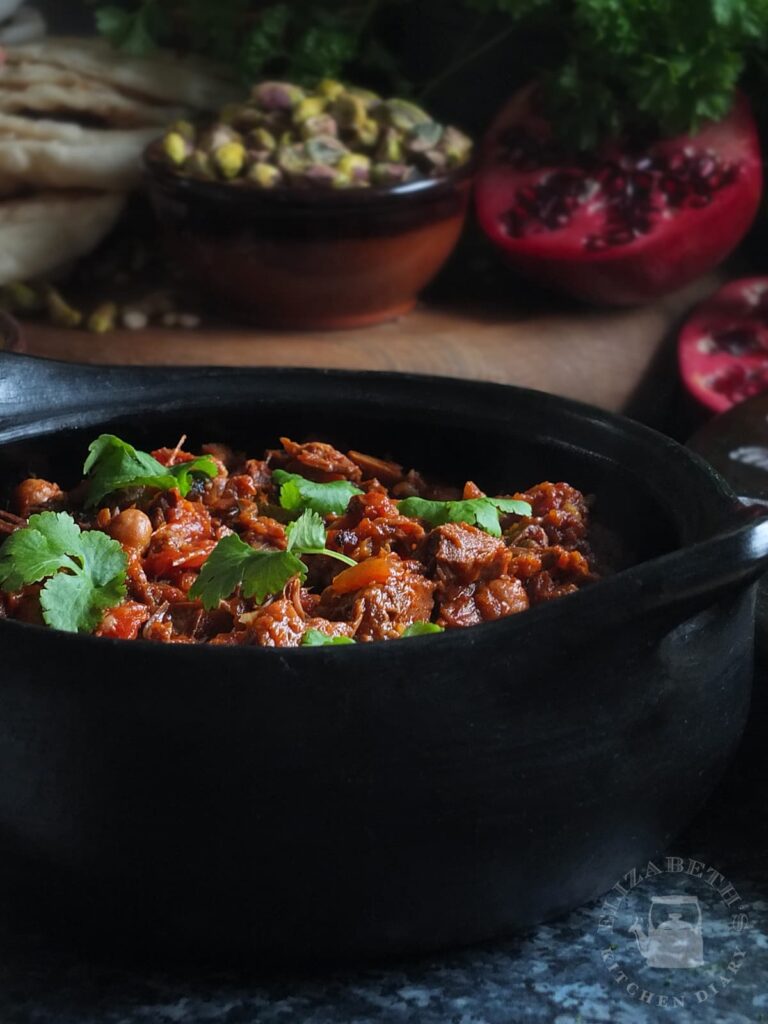 Dark moody image of slow cooked Moroccan lamb shoulder in a black clay pottery cooking dish.