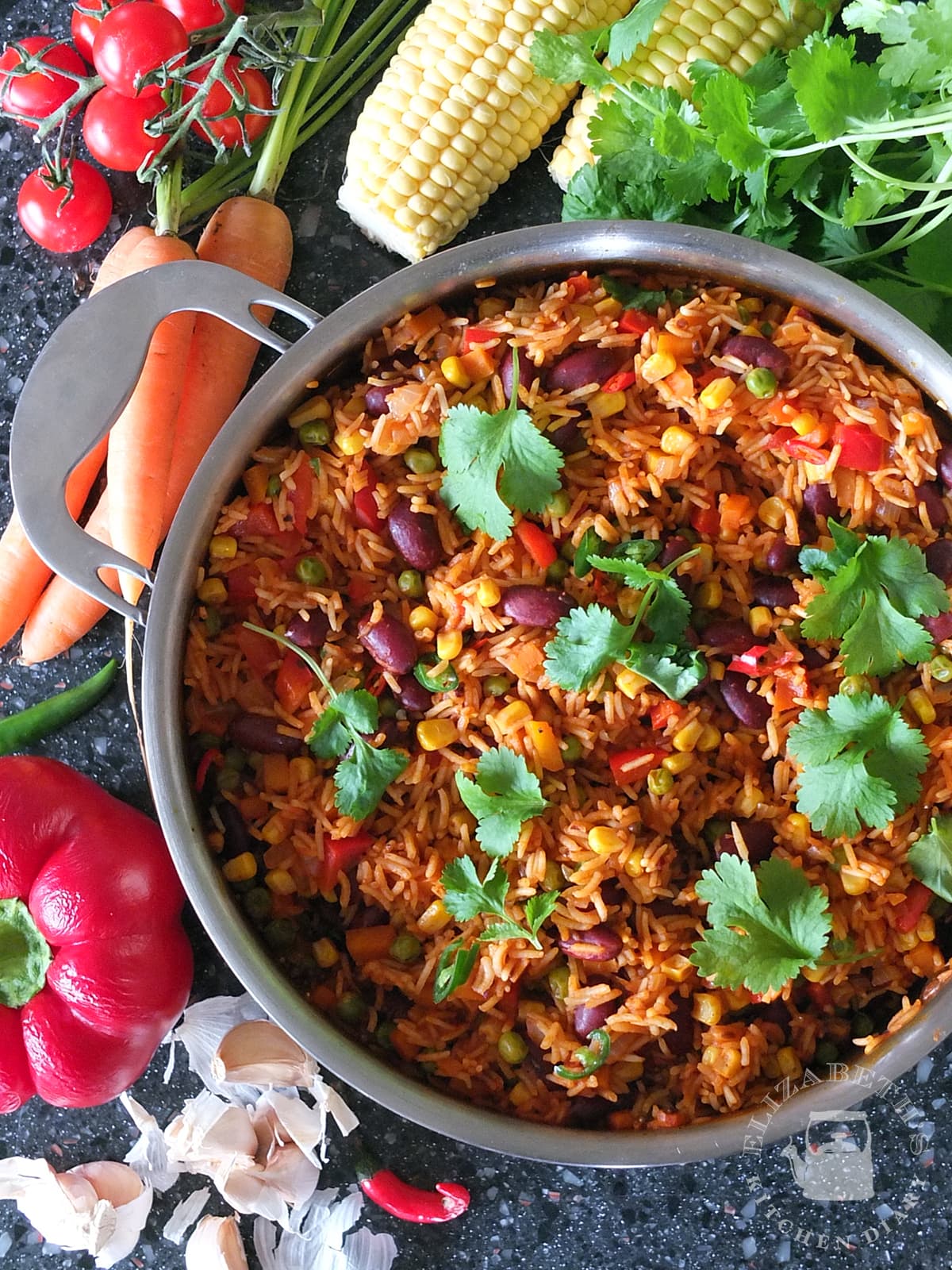 Top down photo of Mexican rice in a large saute pan surrounded by fresh vegetables.