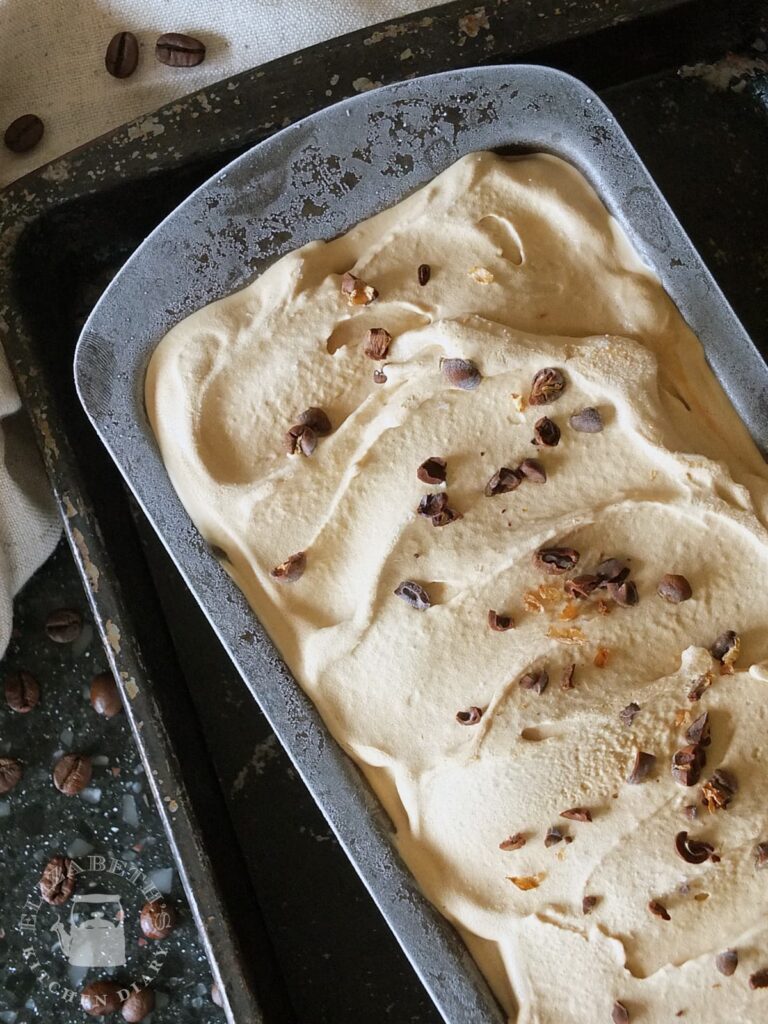 Top down close up of coffee ice cream in a bread tin with finely chopped cocoa beans sprinkled on top.