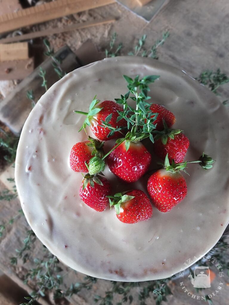 A top down image of fresh strawberries and thyme sprigs decorating a birthday cake.