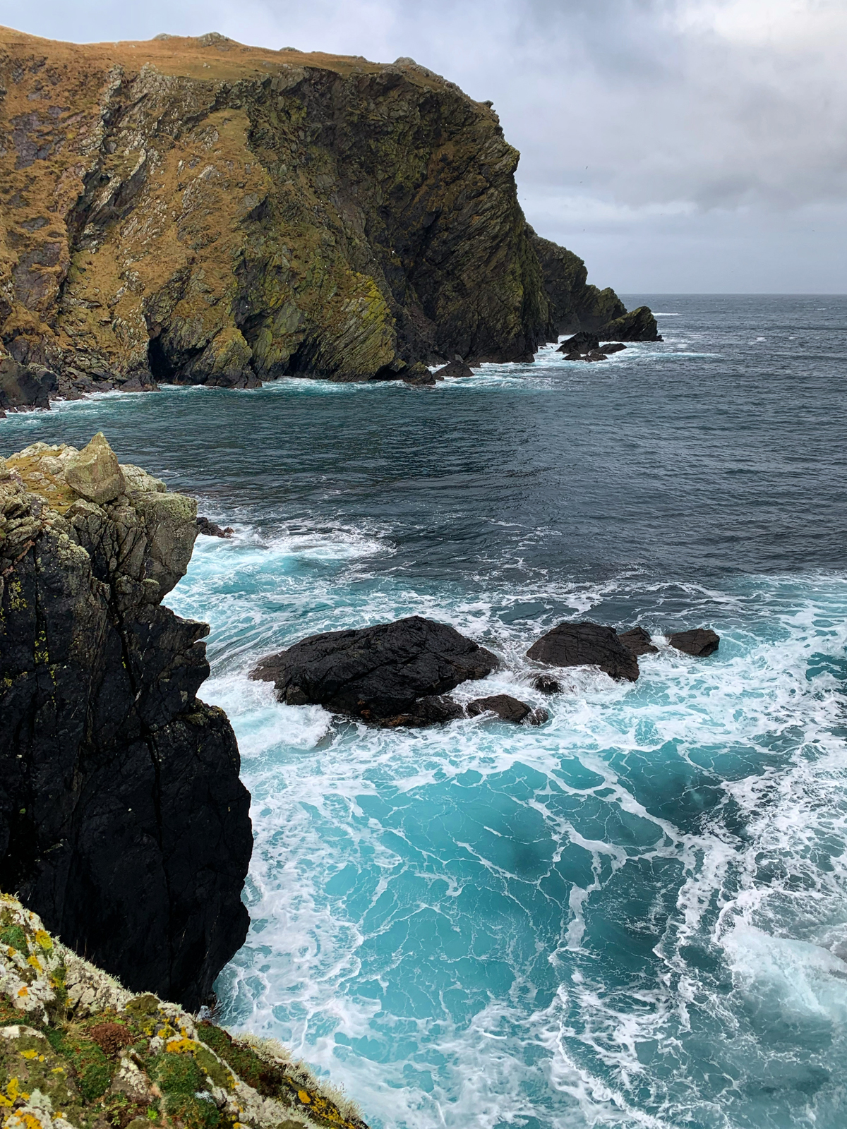Photo of the cliffs at The Face of Neeans with a vibrant blue sea at its base.