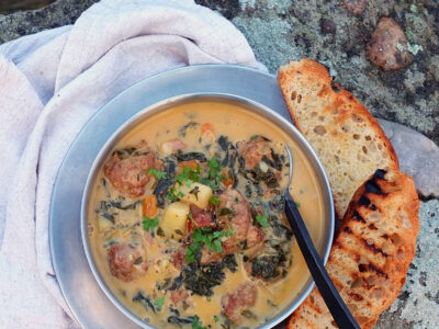 Image of a stainless steel camping bowl filled with chorizo chowder. There are a few slices of toasted focaccia on the side with gorgeous black grill lines.