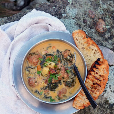 Image of a stainless steel camping bowl filled with chorizo chowder. There are a few slices of toasted focaccia on the side with gorgeous black grill lines.