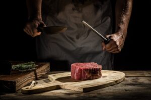 Elizabeth's Kitchen Diary category image for meat and poultry recipes showing a man sharpening a knife over a raw piece of steak.