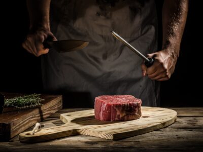 Elizabeth's Kitchen Diary category image for meat and poultry recipes showing a man sharpening a knife over a raw piece of steak.