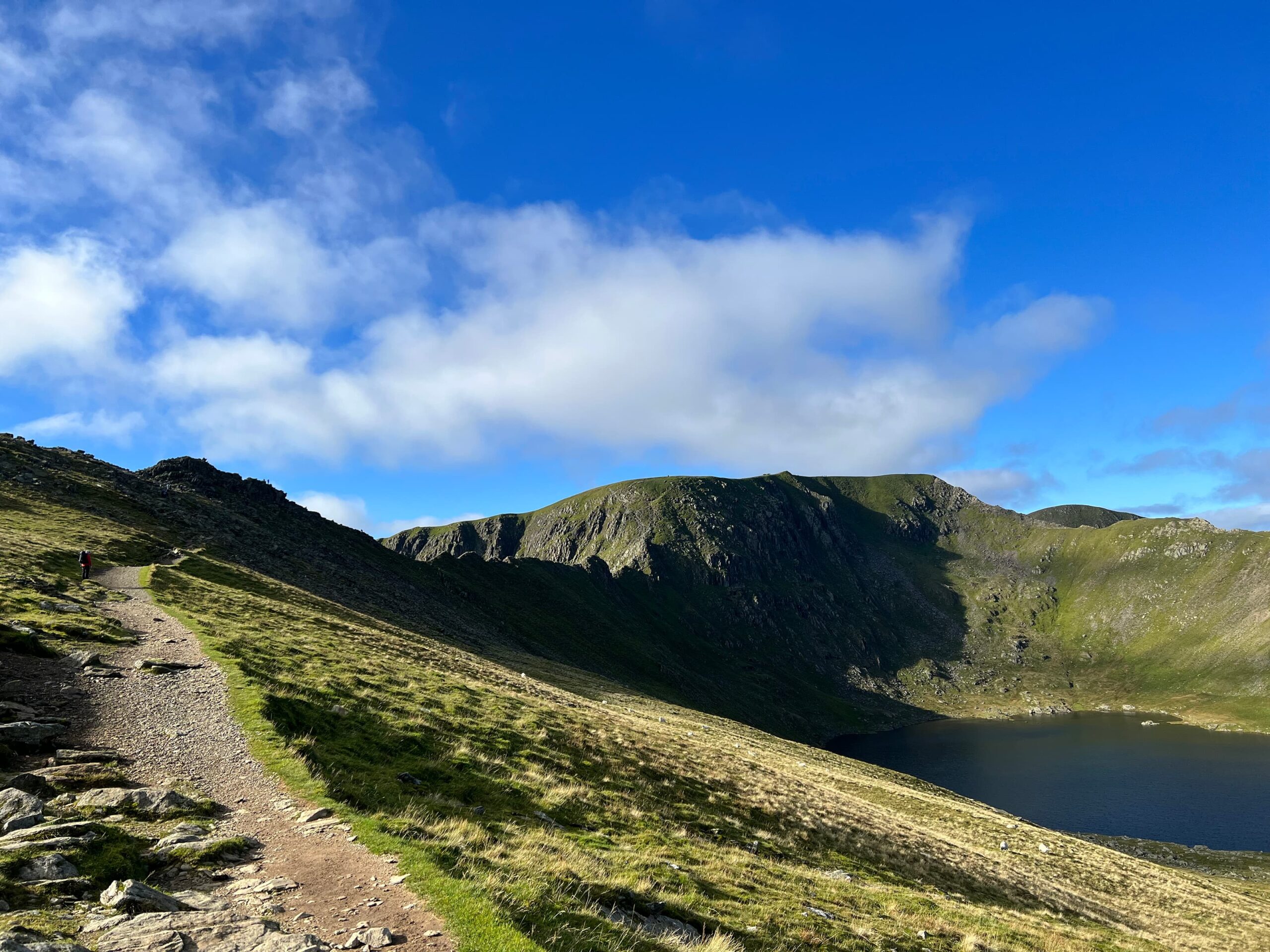 Image of a gravel path leading to the start of the traverse across Striding Edge. Helvellyn is in the background and you can see the Red Tarn lake below.