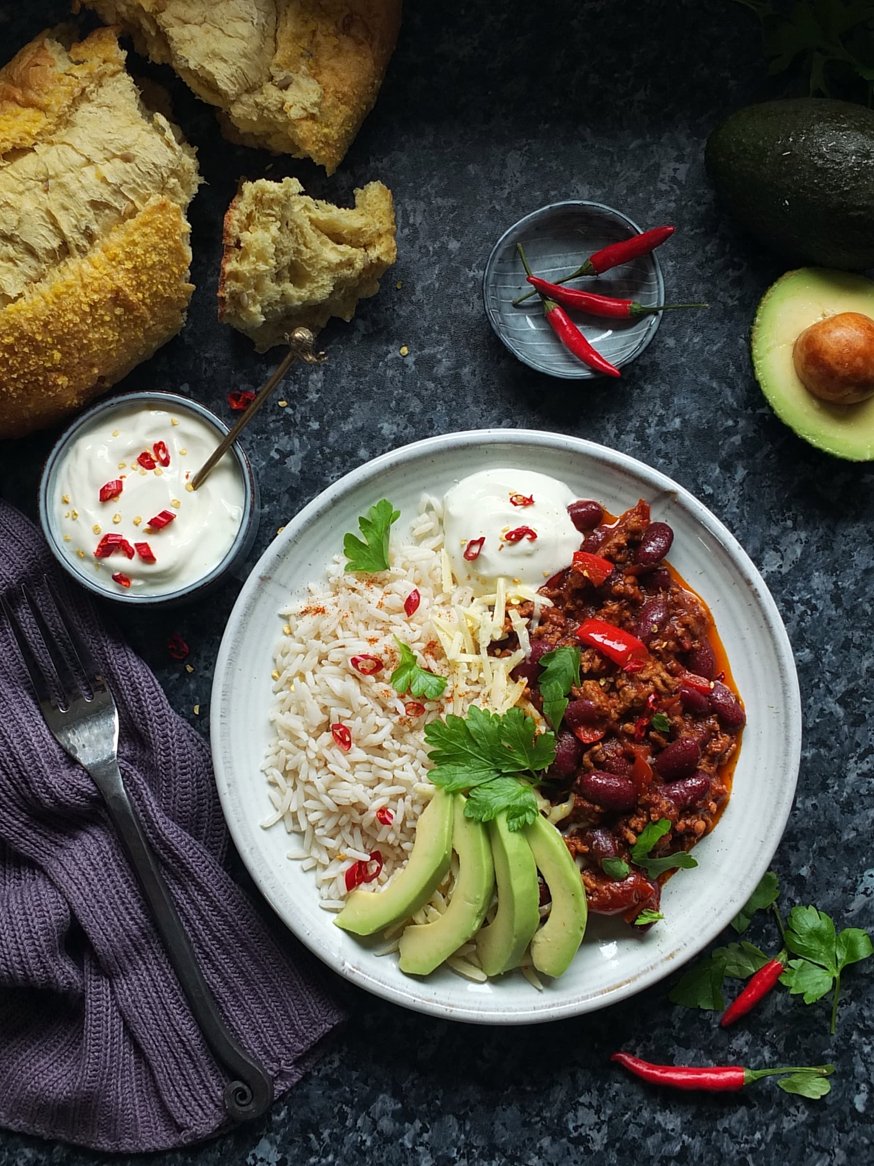 Top down image of lamb chilli con carne served with rice, soured cream, cheddar cheese and avocado.