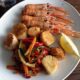 Top down image of pan-seared scallops and langoustines with stir-fried vegetables on a white plate.