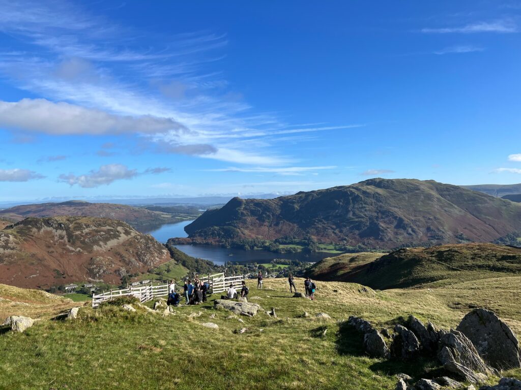 Image of a group of people taking a rest mid-way up the hill climb on Mires Beck. You can see Ullswater in the distance, and some of the large hills in the Lake District.