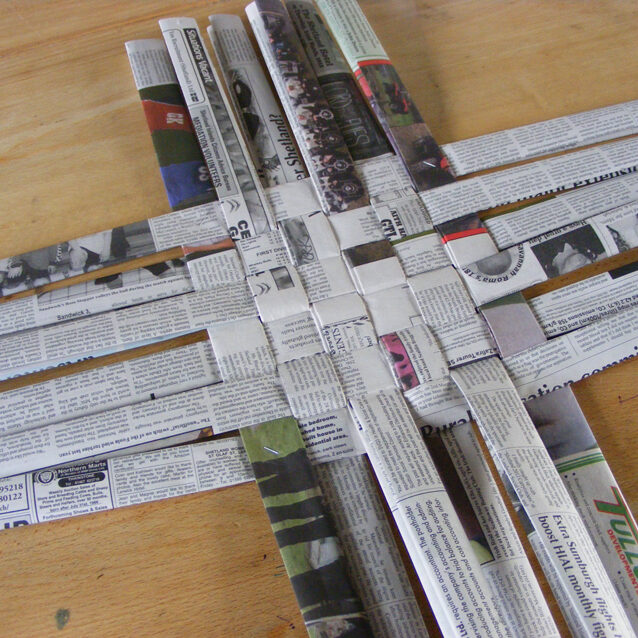 Image of 12 one inch thick strips of folded newspaper woven to make a six inch square woven base.