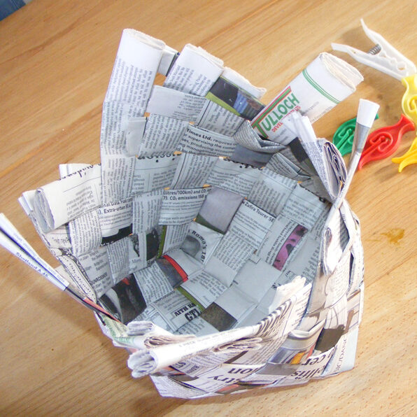 Image of woven newspaper shaped into a rough basket shape.