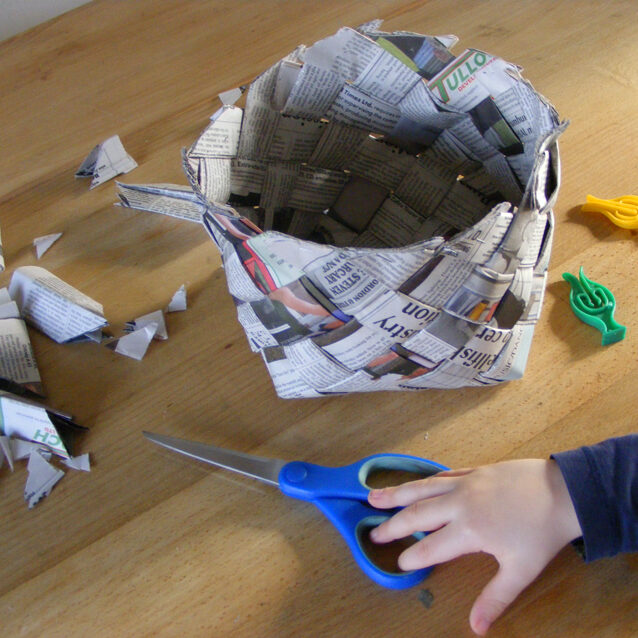Image of woven newspaper shaped into a basket shape with the edges trimmed.
