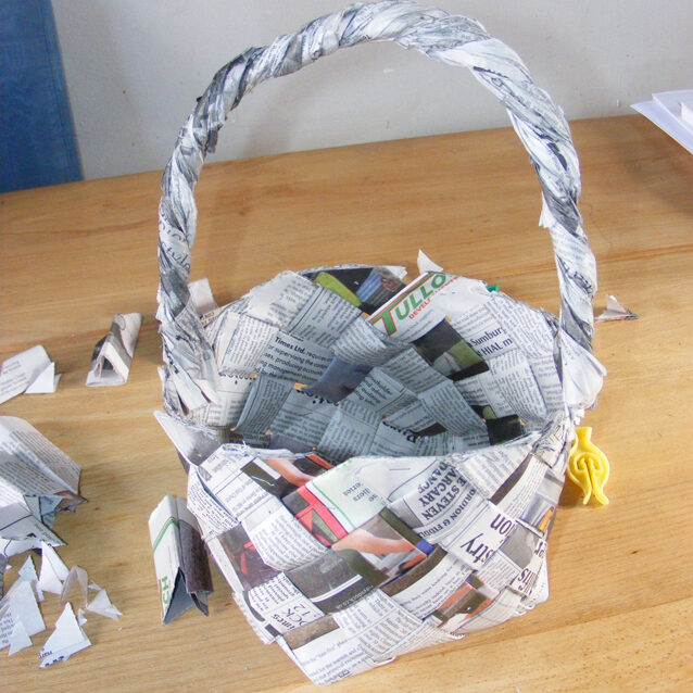 Image of a rough woven newspaper basket with a newspaper handle stapled on.