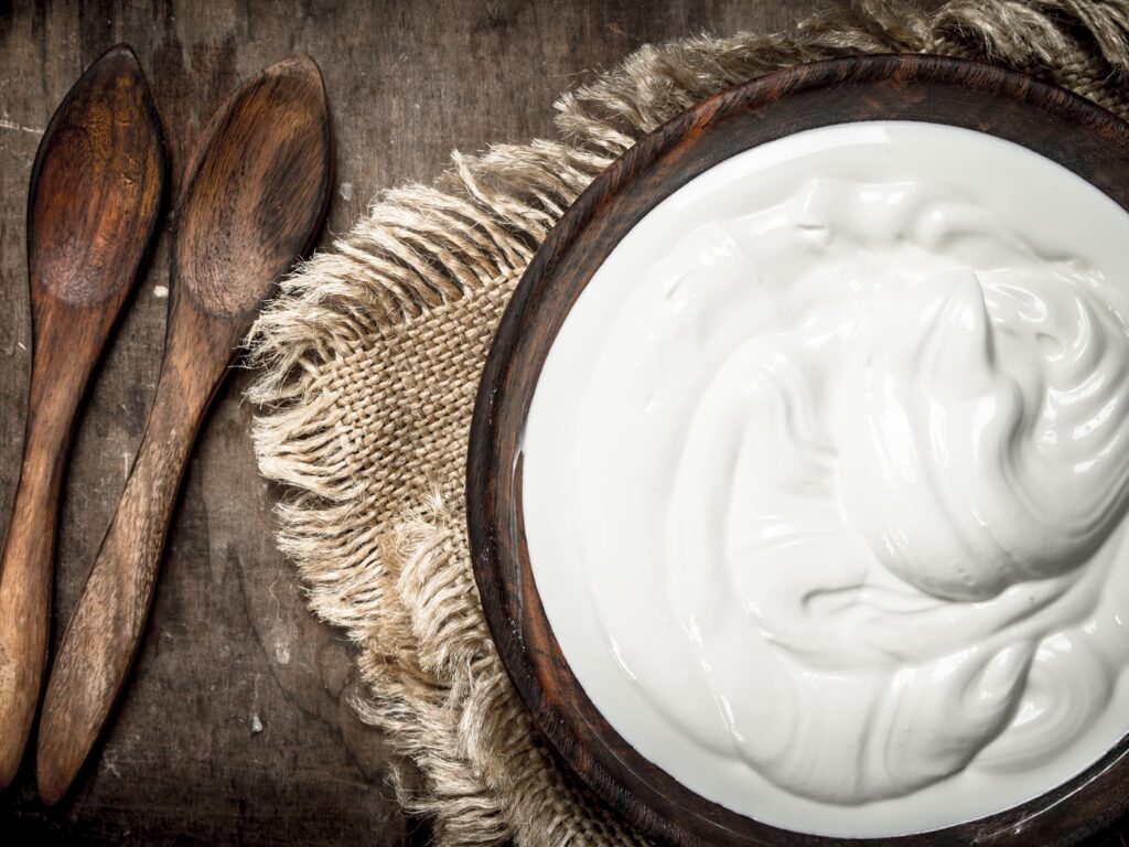 Image of a wooden bowl filled with yoghurt and two wooden spoons at the side.