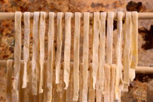 Image of ribbons of fresh pasta drying on a wooden rail.