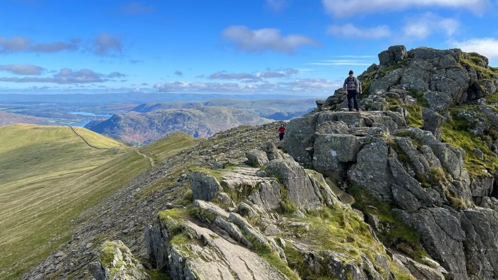 Image of scramblers along Striding Edge with the lakes and hills of the Lake District in the distance.
