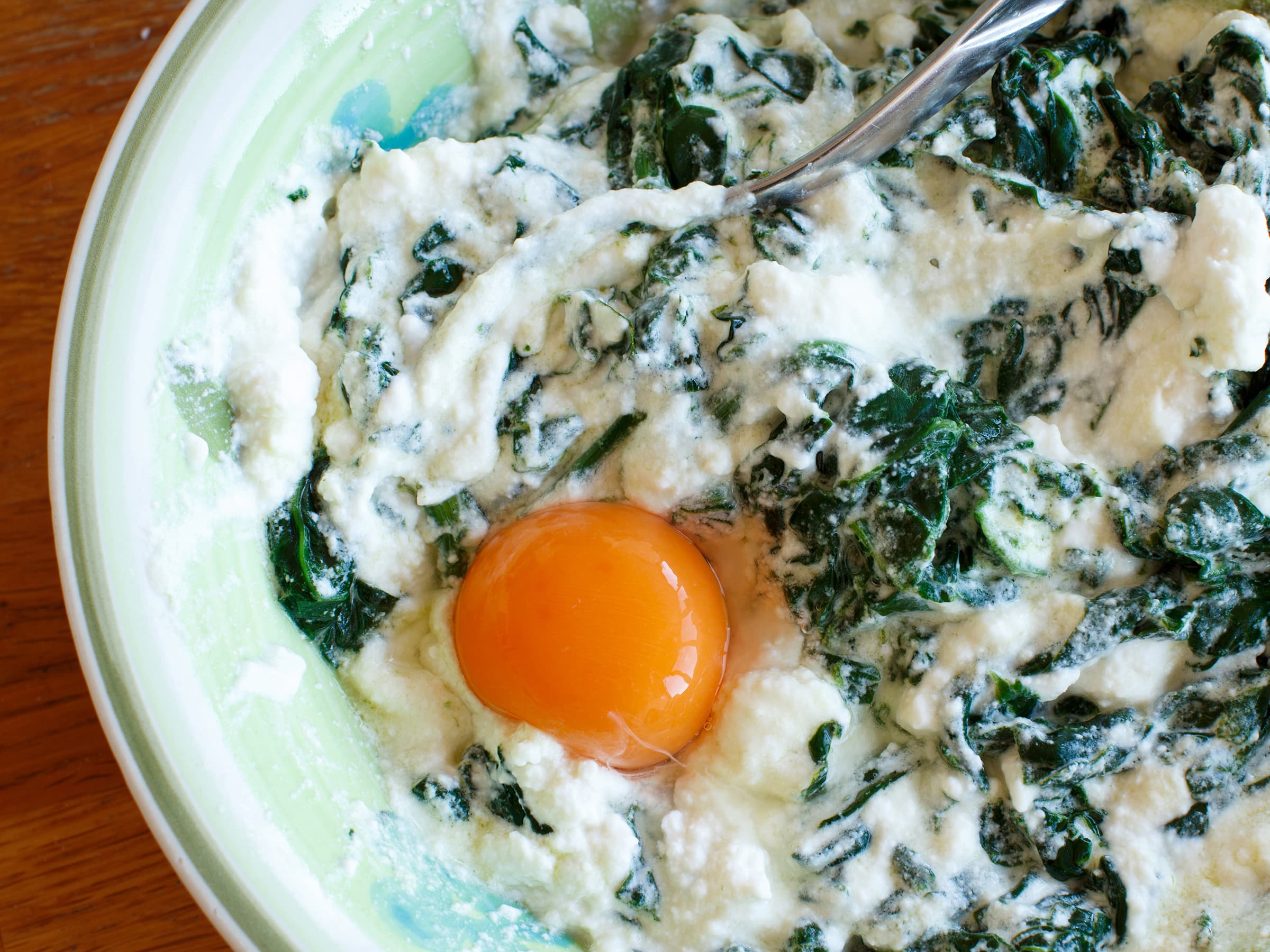 Close up image of an egg yolk in a bowl of spinach and ricotta.