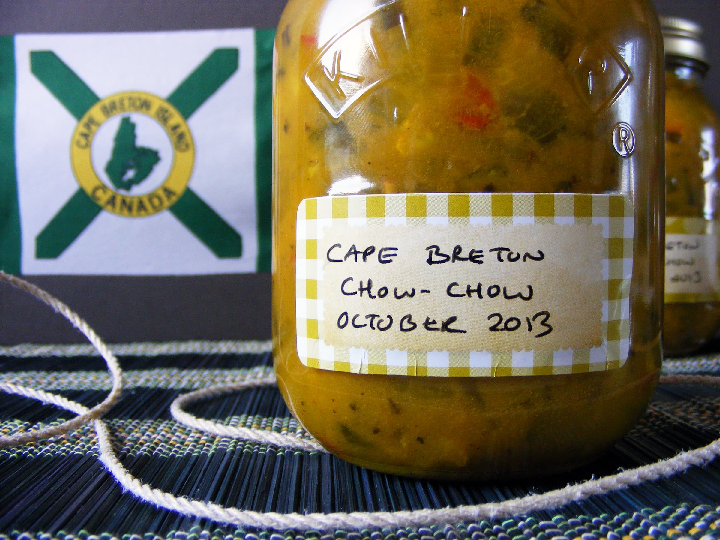 Close up image of a jar of cape breton chow chow, with the cape breton flag in the background.