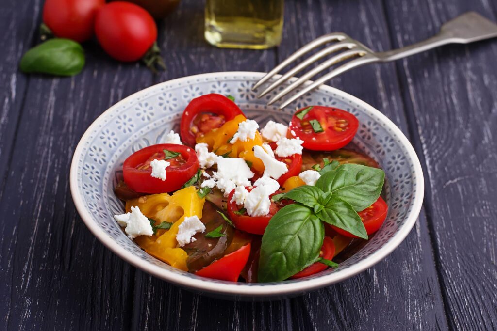 Close up photo of a tomato and goat's cheese salad with an upturned silver fork in the top right hand side. It's bright and inviting.