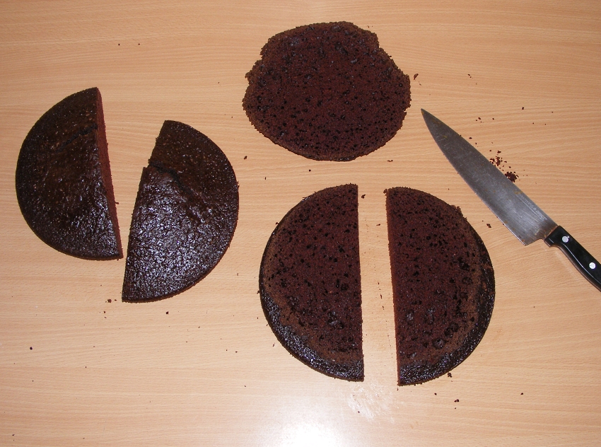 Image of two chocolate cakes cut into half through the middle for a pirate ship. One has the top dome cut off to make it flat.