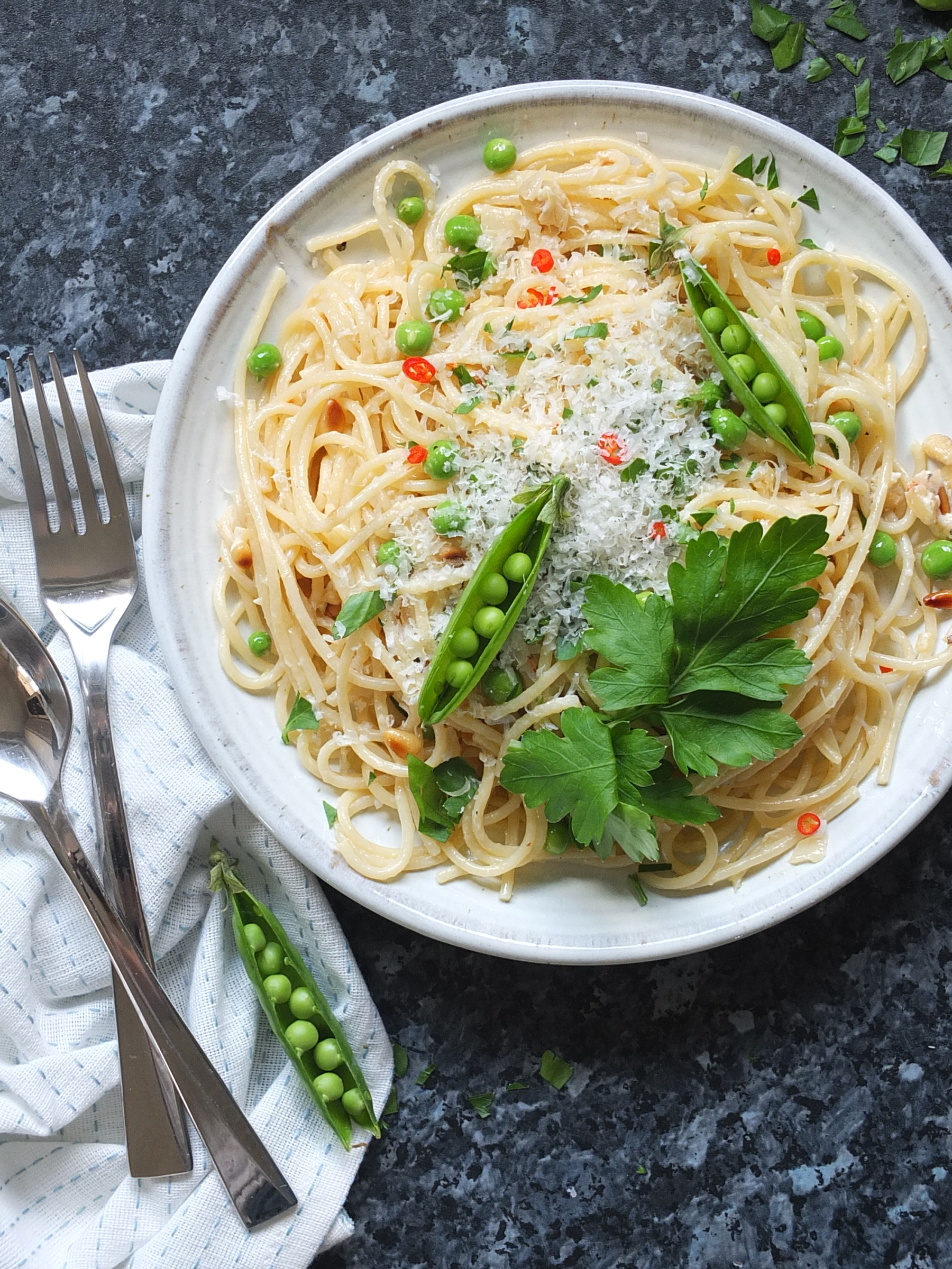 Top down image of a plate of spaghetti on a plate with green peas and grated cheese on top.