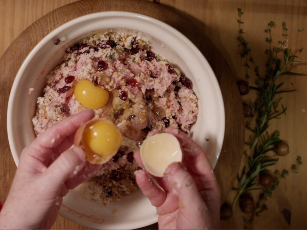 Image of hands cracking eggs into pork stuffing.