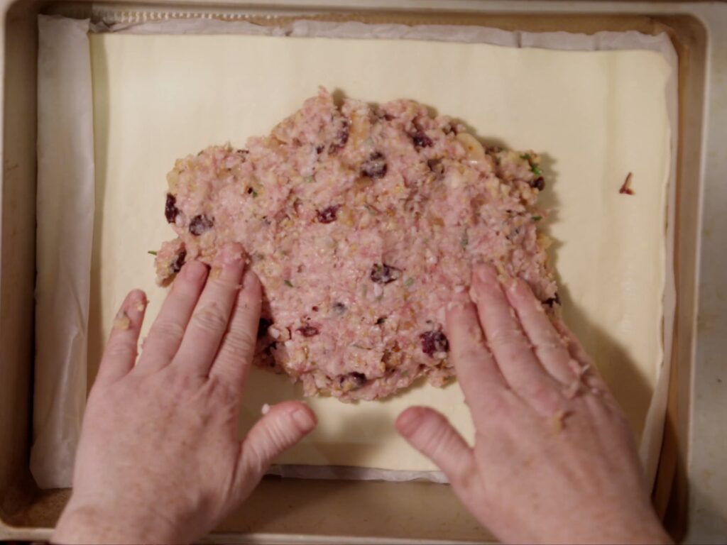 Image of pork sausagemeat spread out onto a layer of puff pastry.