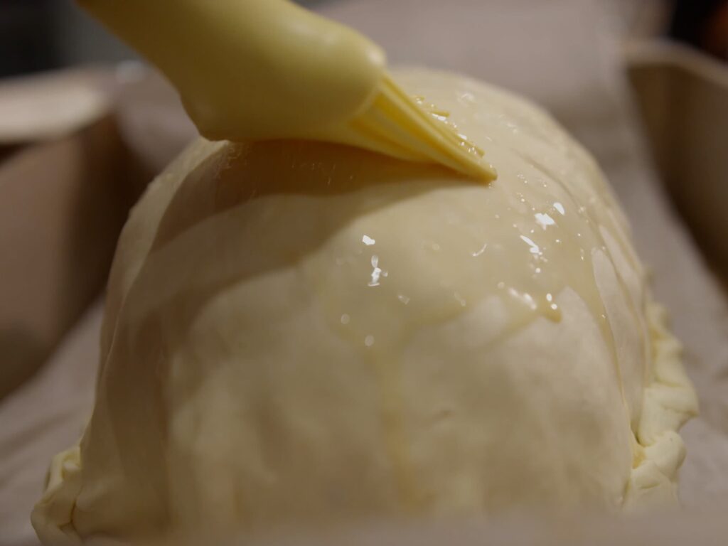Image of pastry brush brushing beaten egg yolk onto puff pastry.